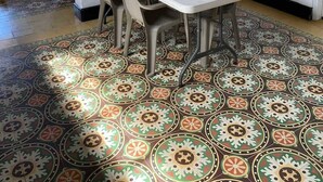 A dining area with a table and chairs, a clock on the wall, and patterned floor tiles. - Believer Hostel (Santa Marta)