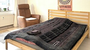 A bedroom with a wooden bed, a brown chair, a hanging light, and a poster on the wall. - Apartment, 10 min. walk to the center, 45m2,Netflix& all amenities! (Erfurt)