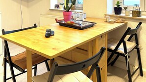 A dining area with a wooden table, four chairs, a television mounted on the wall, and two windows with views of buildings. - Apartment, 10 min. walk to the center, 45m2,Netflix& all amenities! (Erfurt)