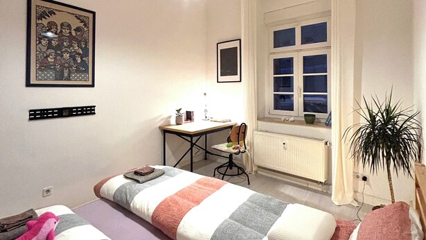 A bedroom with two beds, a desk, a chair, a radiator, a window with curtains, and a plant. - Apartment, 10 min. walk to the center, 45m2,Netflix& all amenities! (Erfurt)