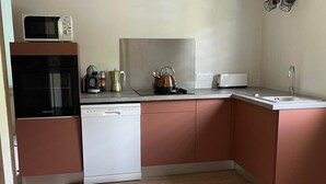 Ett kompakt kök med mikrovågsugn, kaffebryggare, vattenkokare och diskmaskin.