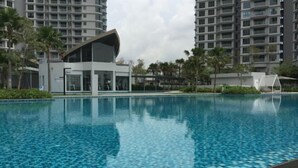 A swimming pool with a tiled floor, surrounded by modern buildings and palm trees. - Teega Residence Waterfront Living (Iskandar Puteri)