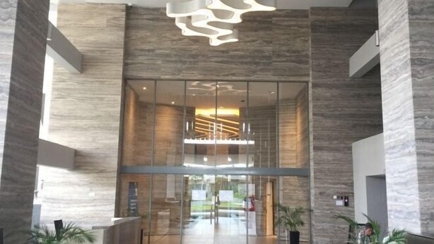 A modern lobby with a glass entrance, a unique ceiling light fixture, and a view of the outdoor area. - Teega Residence Waterfront Living (Iskandar Puteri)