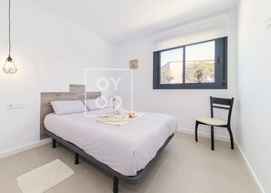 Een slaapkamer met een bed, een stoel, een raam en een hanglamp.