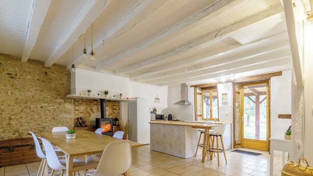 A spacious kitchen with a central island, white walls, exposed wooden beams, and a stone wall on one side.