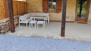 A covered outdoor seating area with a stone wall, wooden door, and a view of the outdoors.