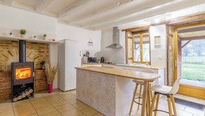 A kitchen with a wood-burning stove, a refrigerator, a microwave, and a bar area with stools.