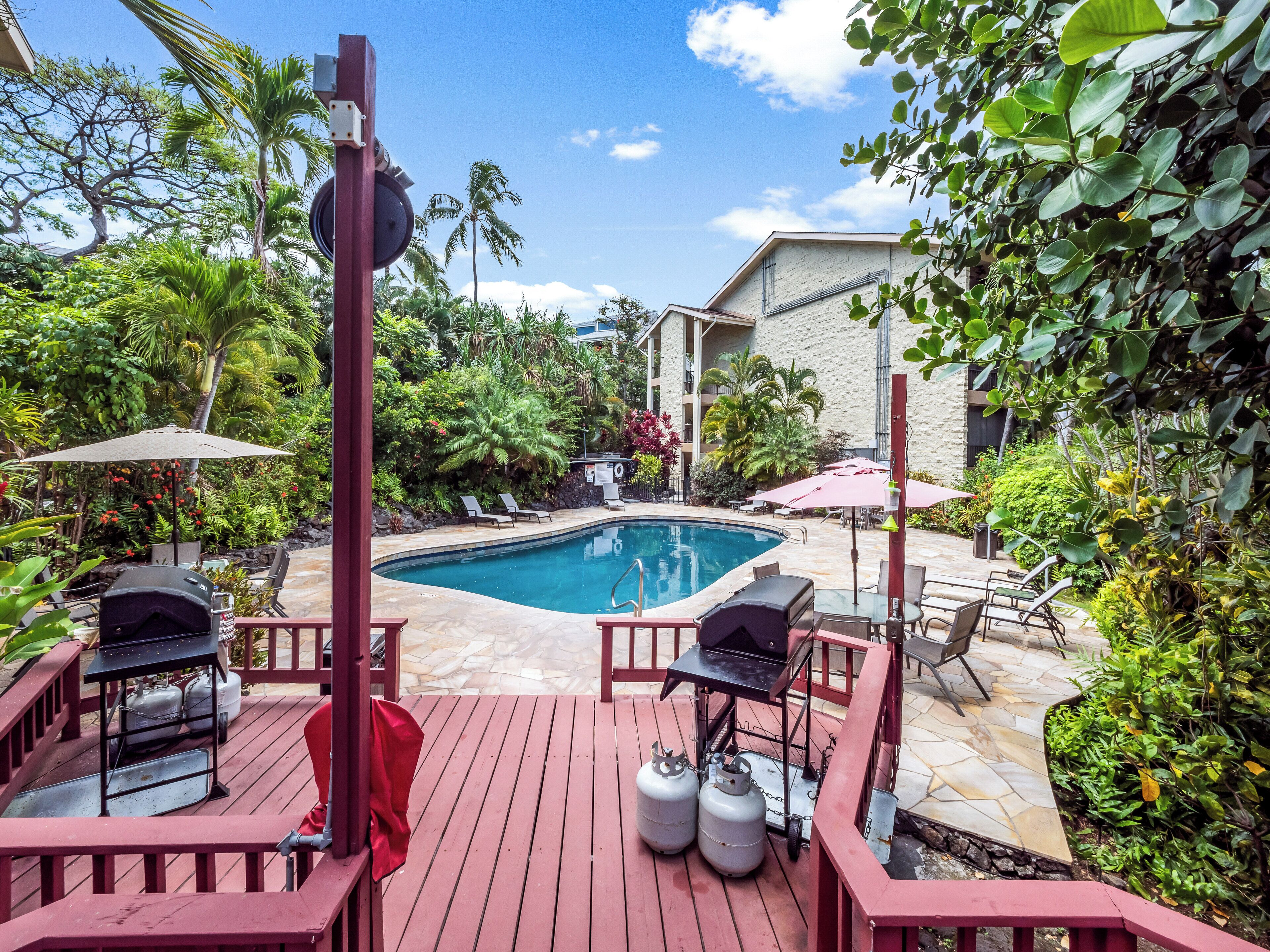 A pool area with a wooden deck, lounge chairs, and a barbecue grill.
