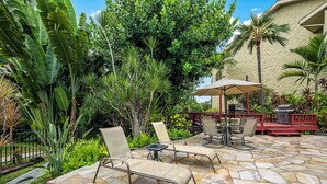An outdoor patio with stone flooring, lounge chairs, a table, and an umbrella. - Kalanikai 118 Highly Walkable! (Kailua-Kona)