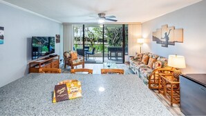 A hotel room with a kitchen area, dining table, and chairs. There is a television, a refrigerator, and a dining area with a view of the outdoors. - Kalanikai 118 Highly Walkable! (Kailua-Kona)
