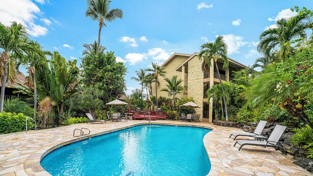 A swimming pool with stone tiles, surrounded by lounge chairs and palm trees. - Kalanikai 118 Highly Walkable! (Kailua-Kona)