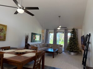 Un salon comprenant un coin repas, un ventilateur de plafond, un sapin de Noël et une grande fenêtre avec des rideaux.