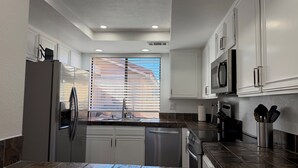 A modern kitchen with white cabinets, a stainless steel refrigerator, a dishwasher, and a microwave. - Luxury 2BR/2BA Smart Home in Monterey Country Club – Palm Desert, CA (Palm Desert)
