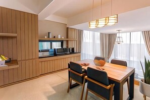 A modern kitchen with wooden cabinetry, a dining table with chairs, and a pendant light. - Sky Hill Villa Surattthani (Surat Thani)