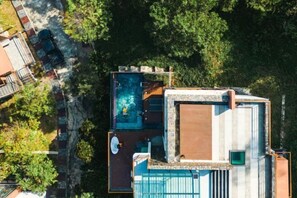 A rooftop pool with a view of surrounding trees and a building with a stone facade. - Sky Hill Villa Surattthani (Surat Thani)