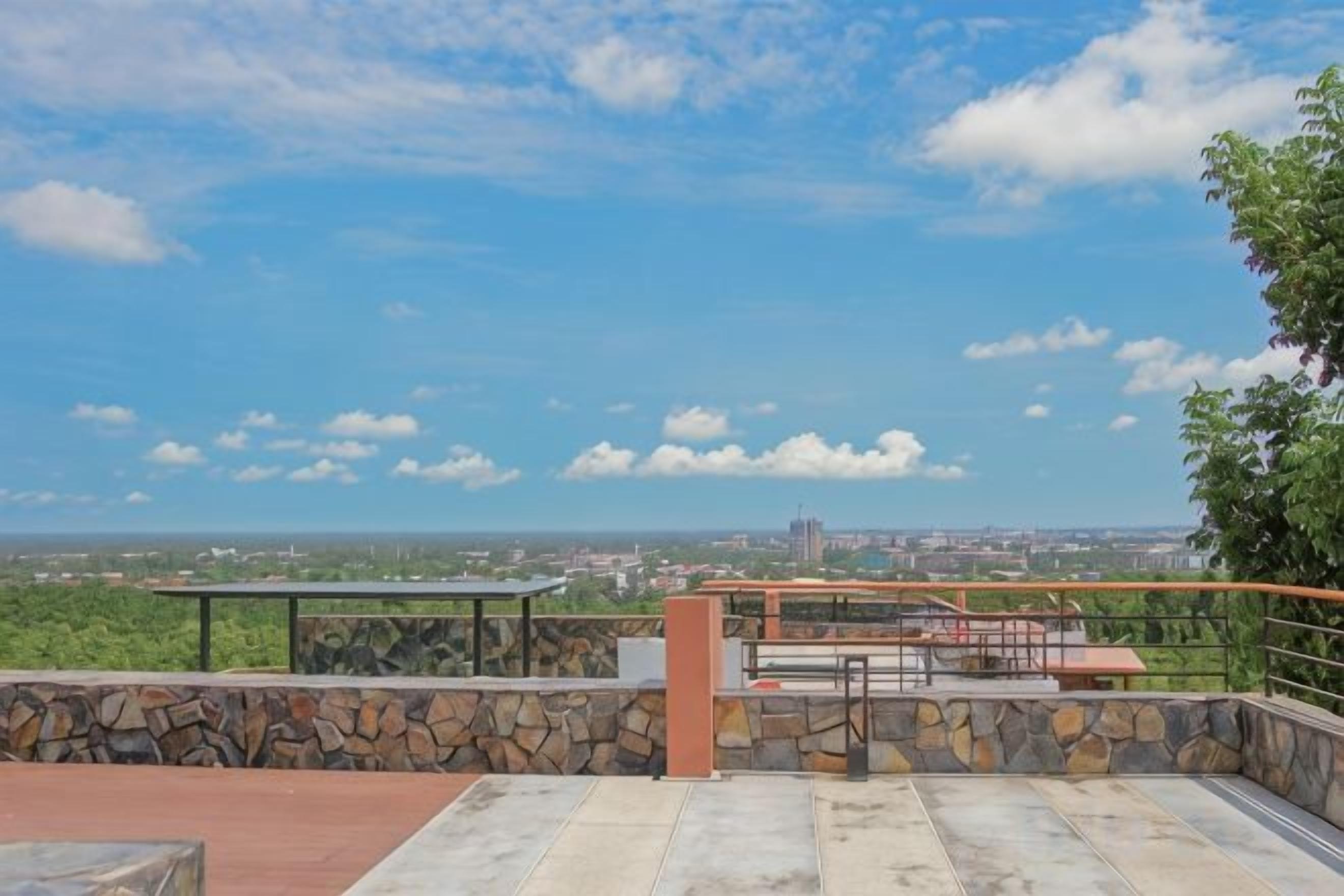 Une terrasse sur le toit, avec un mur en pierre, une rambarde en métal et une vue sur le paysage urbain.