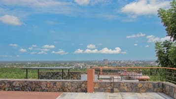 A rooftop terrace with a stone wall, a metal railing, and a view of a cityscape.
