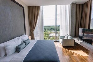 A modern hotel room with a large bed, a TV, and a view of the city. - Sky Hill Villa Surattthani (Surat Thani)
