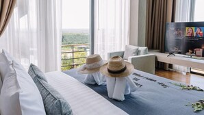 Habitación de hotel moderna con una cama grande, televisión y balcón con vistas al follaje.