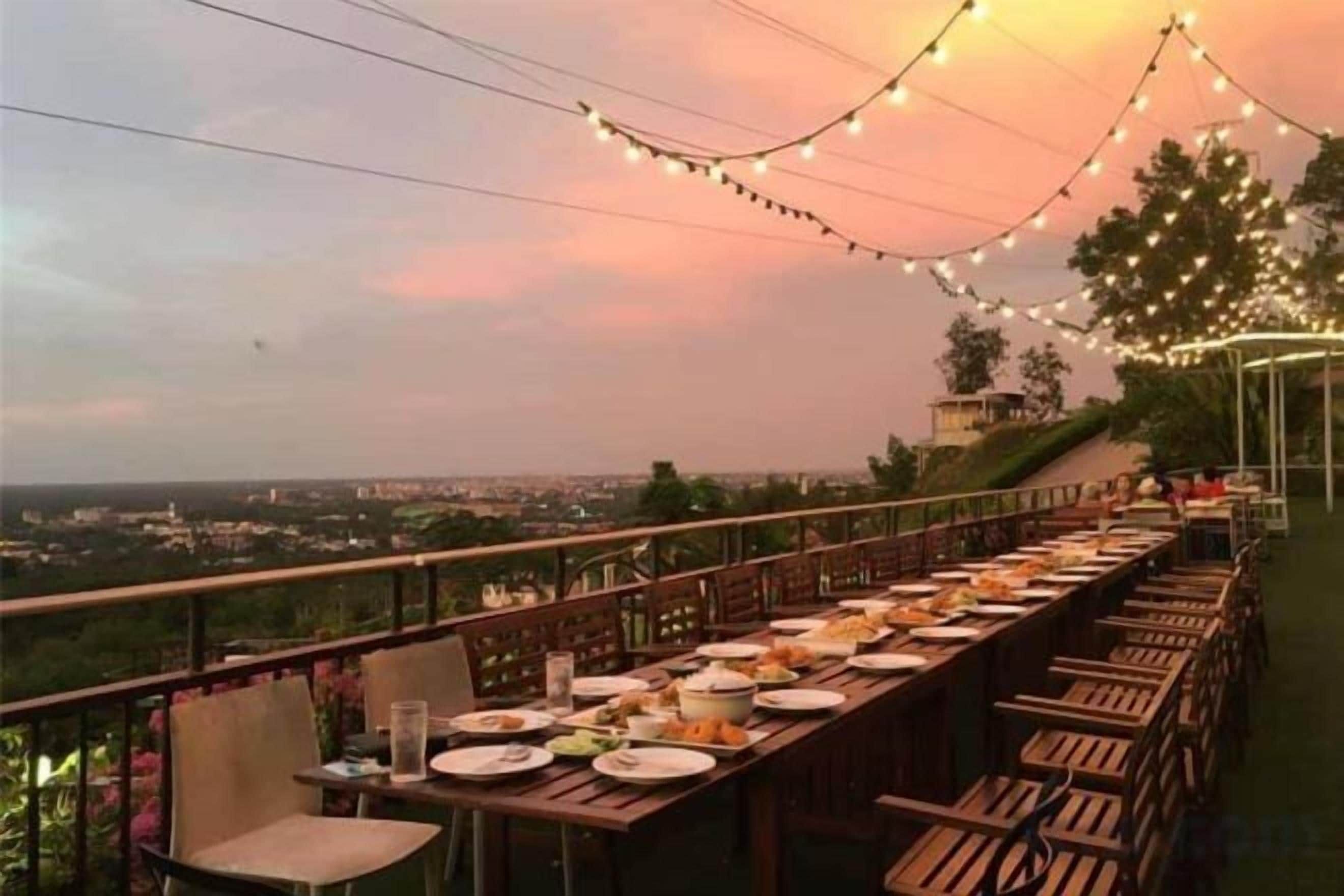 An outdoor dining area with tables and chairs, string lights, and a view of the city.