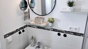 Ein Badezimmer mit einem weißen Waschbecken, zwei Spiegeln, einer kleinen Ablagefläche mit einer Pflanze und einer Toilette.