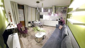 Un salon moderne avec un canapé gris, un fauteuil violet, une table à manger avec des chaises et une petite table blanche ornée d’une plante.
