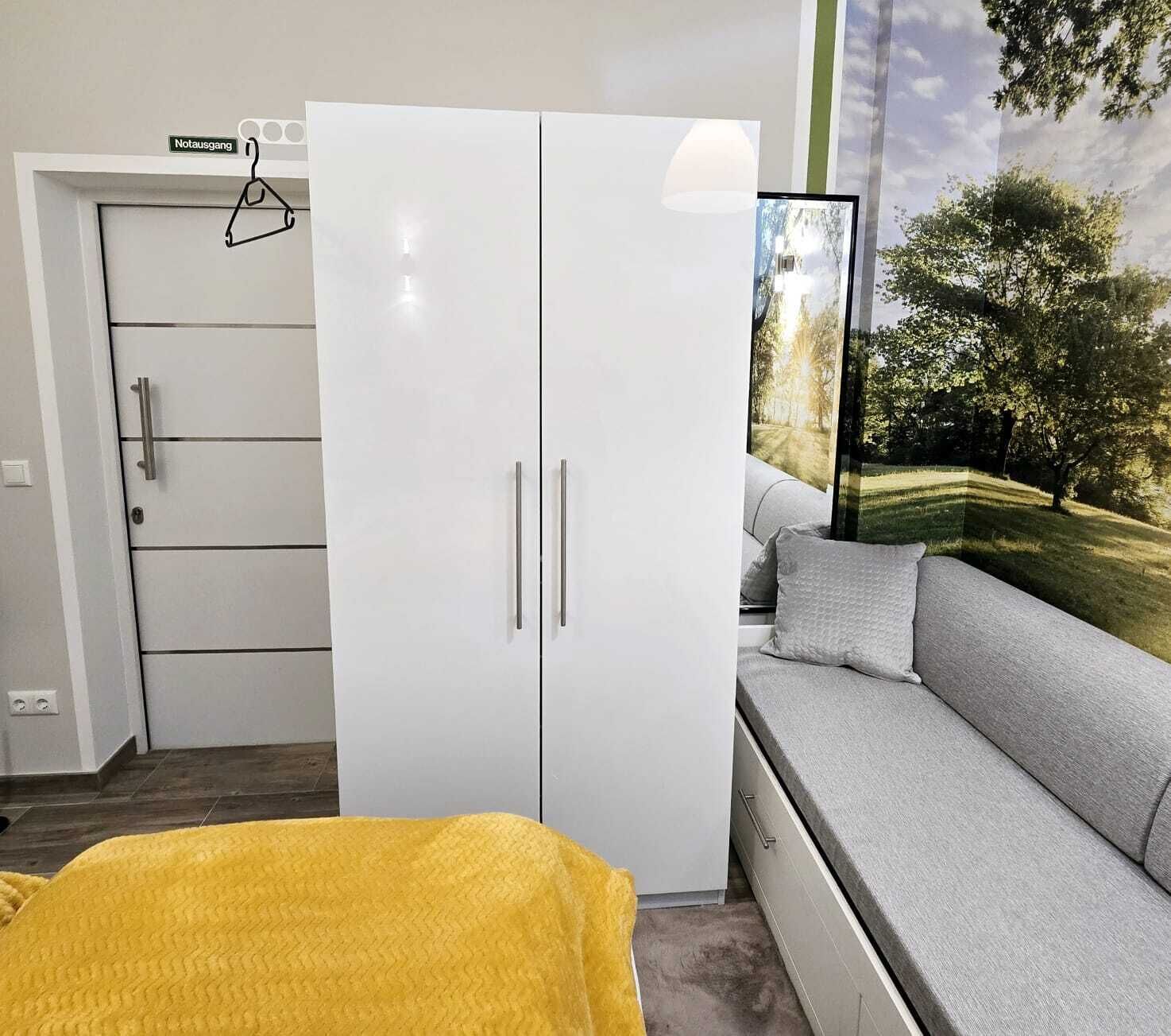 Ein Zimmer mit einem weißen Kleiderschrank, einem grauen Sofa und einer gelben Decke.