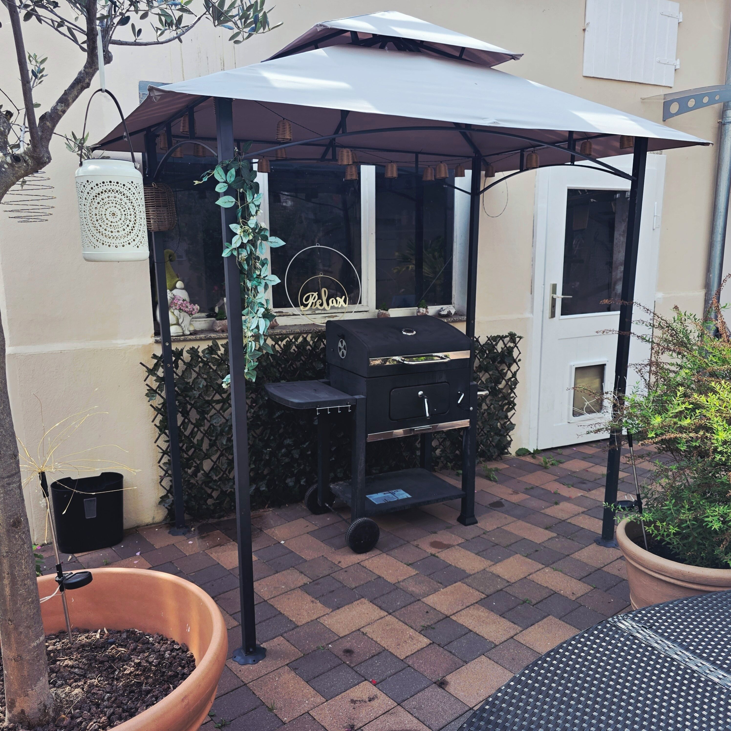 A patio area with a barbecue grill under a canopy, a potted plant, and a tiled floor.