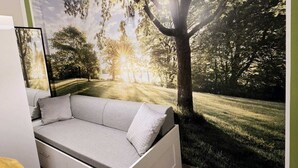 Une chambre dotée d’un canapé-lit intégré, d’une petite table de chevet et d’une grande fenêtre donnant sur un parc.