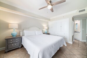 Une chambre à coucher comprenant un lit, des tables de chevet, un ventilateur de plafond et un dressing.