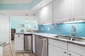 Eine Küche mit weißen Schränken, einem Edelstahl-Spülbecken und einer blauen Mosaikrückwand.