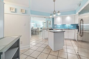 A modern kitchen with white cabinetry, a central island, and a blue backsplash.