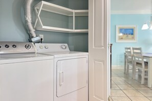 A laundry area with a washing machine and dryer, a vent pipe, and a dining area in the background. - Summer House 905A | Gulf Front | Resort Amenities | My Beach Getaways (Orange Beach)