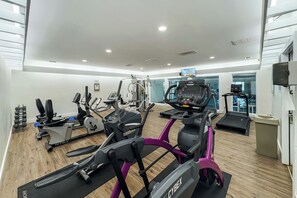 Une salle de sport moderne équipée de machines de cardio, de postes d’entraînement avec poids et d’un écran de télévision.