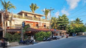 Un immeuble de deux étages doté d’un balcon, un restaurant avec une terrasse, et plusieurs motos garées.
