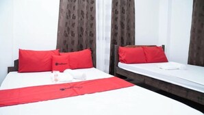Une chambre d’hôtel avec deux lits, chacun étant agrémenté d’un oreiller rouge et d’une couverture blanche.