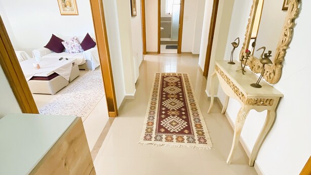 A hallway with a wooden floor, a patterned rug, a white console table with a mirror, and a door leading to another room. - Cozy 2-Bedroom one level house in La Marsa – Perfect Location & Comfort! (La Marsa)