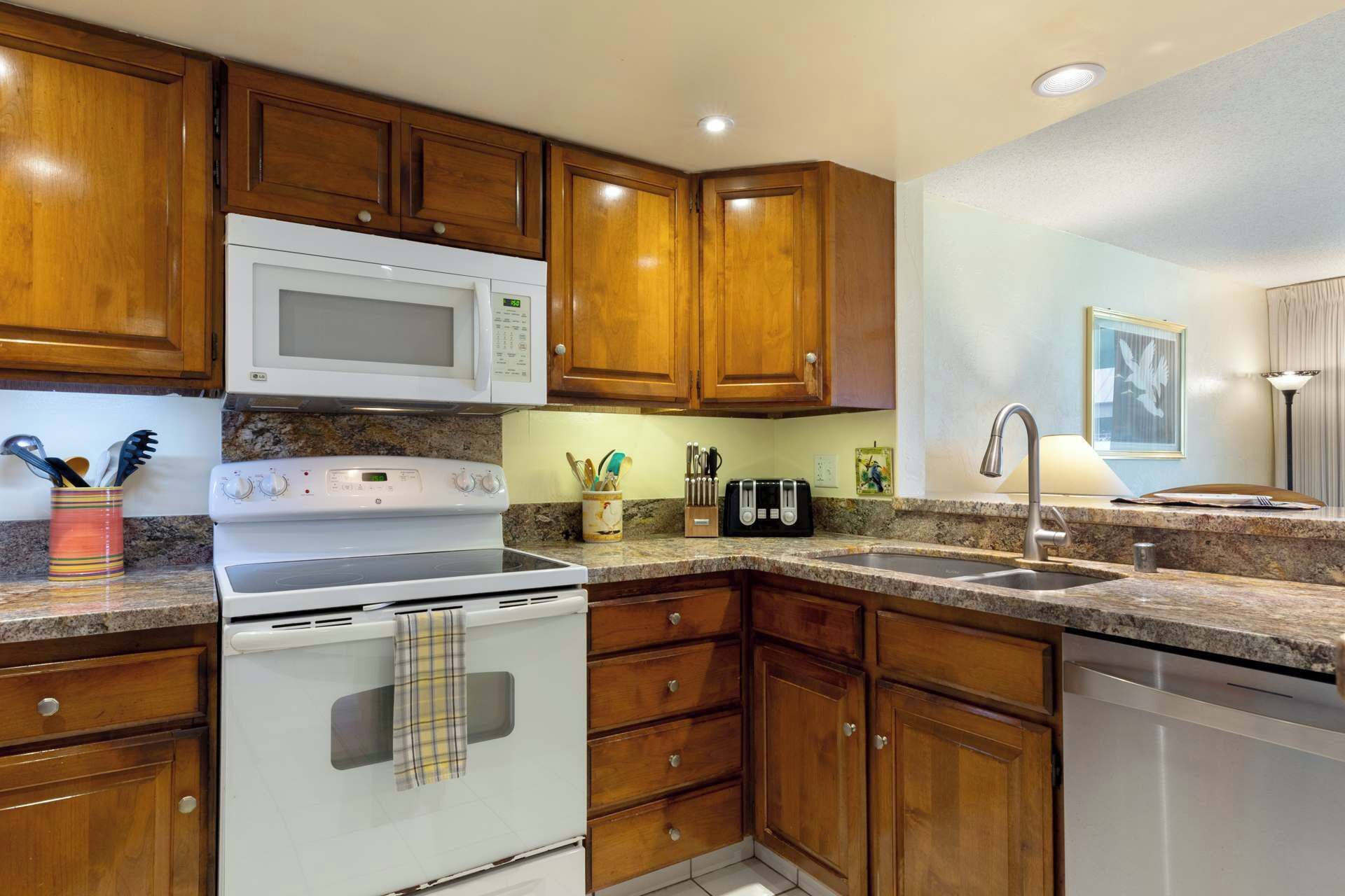 A kitchen with wooden cabinets, a white stove, a microwave, a toaster, and a sink.