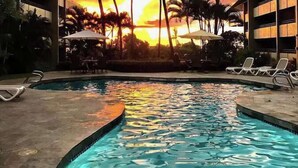 A swimming pool with lounge chairs and palm trees, surrounded by buildings. - White Sands Village 214 Modern Condo for 4 w/ Enviable Ocean Views! (Kailua-Kona)