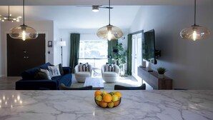 A modern living room with a marble coffee table, a blue sofa, and a dining area with a white table. - Lunar: Old Town Luxury• Heated Pool• 2 Kings• Gameroom• Hottub• Karaoke• Privacy (Scottsdale)