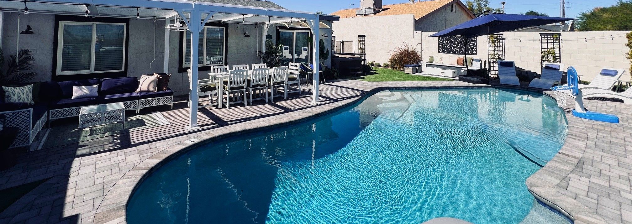 Une piscine dotée d’un espace salon en contrebas, entourée d’une terrasse couverte avec des chaises et des tables.
