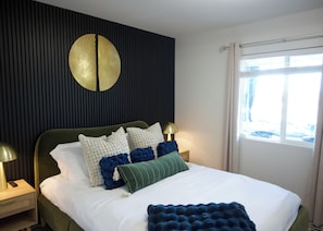 A hotel room with a bed, a round wall decoration, a window with curtains, and a nightstand with a lamp.