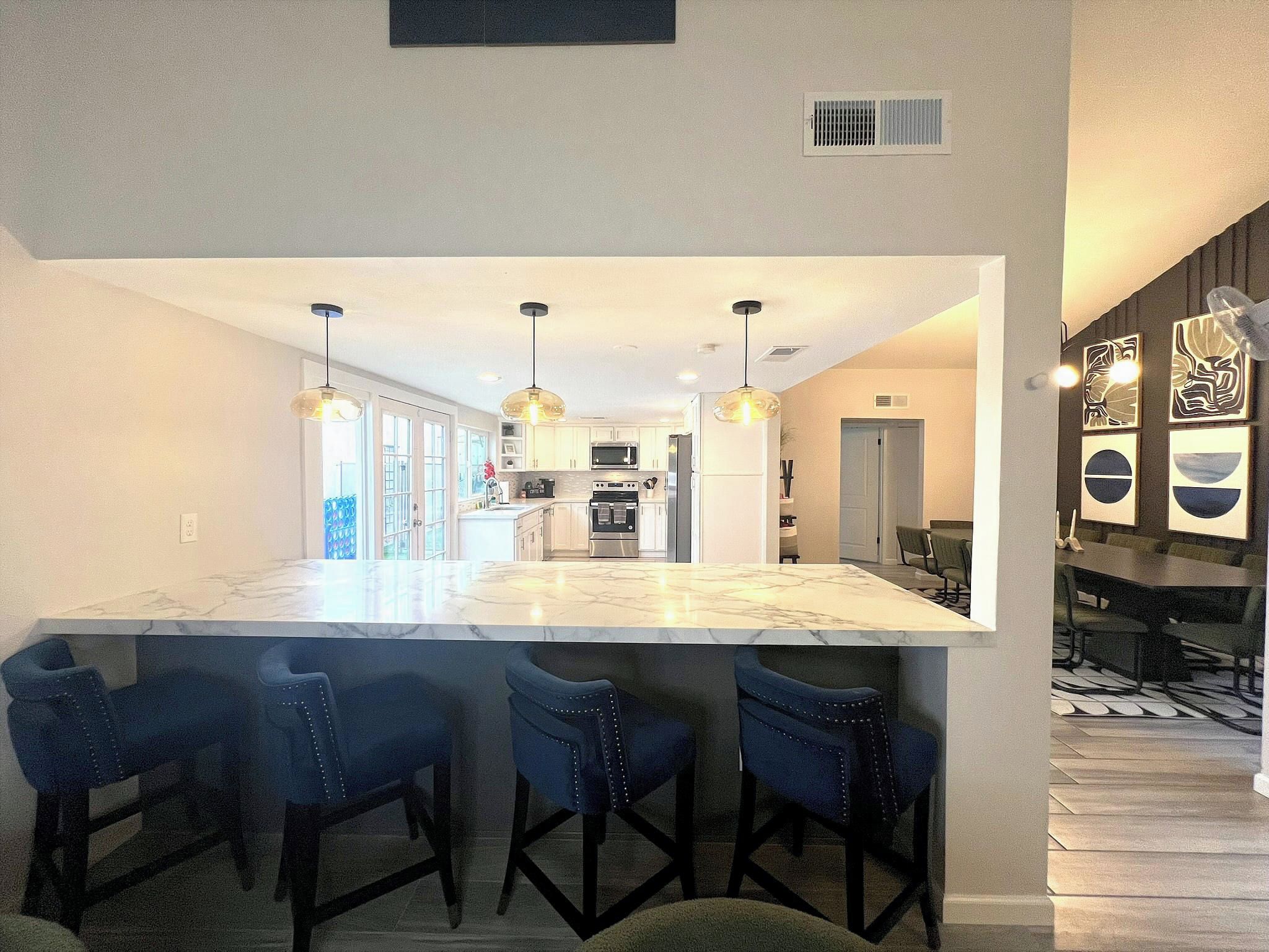 A modern kitchen with a central island, bar stools, pendant lighting, and a dining area with a table and chairs.