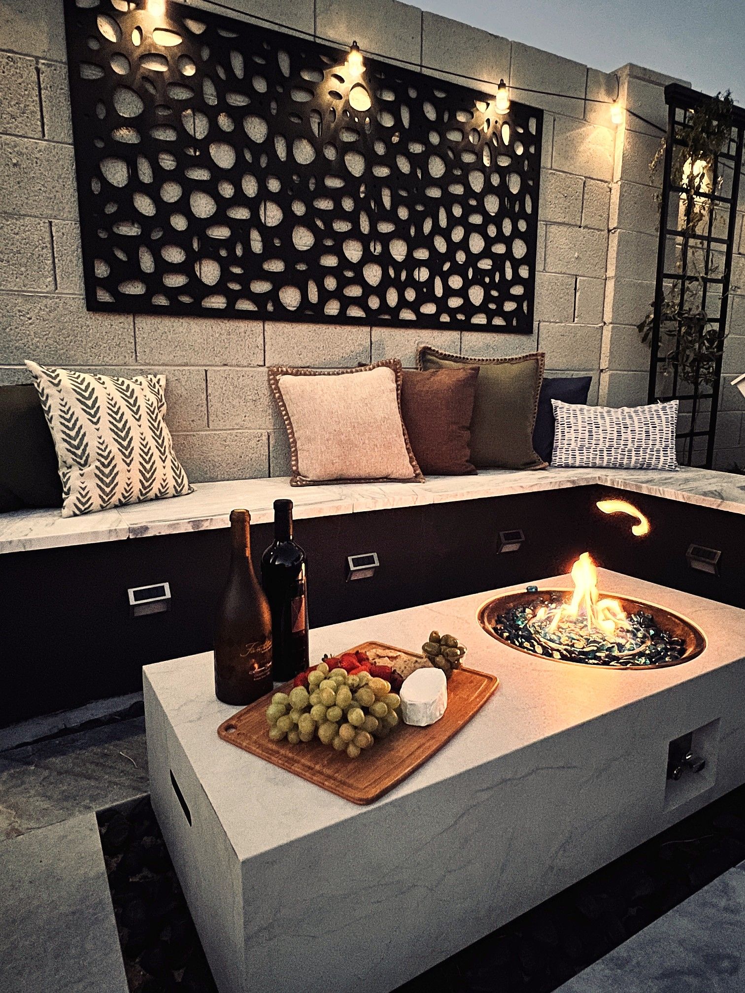 An outdoor seating area with a built-in fire feature, a wine bottle, and a fruit platter.