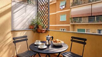 Ein Balkon mit zwei Stühlen, einem Tisch, einer Kaffeemaschine, Tassen und einer Schüssel Croissants.