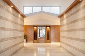 A hallway with a high ceiling, wooden paneling, and a large window.