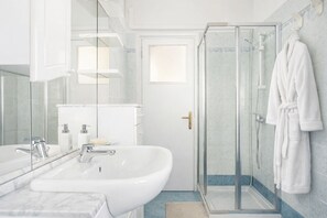 Une salle de bain moderne avec un grand lavabo blanc, une douche en verre et un peignoir blanc accroché au mur.
