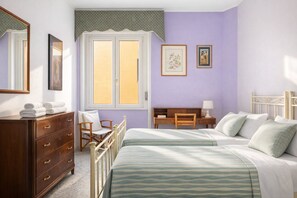 Une chambre avec deux lits, une commode, une chaise, un bureau et une fenêtre avec des rideaux.