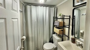 A compact bathroom with a toilet, a white sink, a mirror, and a shower curtain.