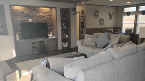 Una sala de estar con un sofá gris, una mesa de centro y un televisor instalado en una pared de piedra.